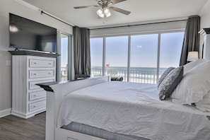 A bedroom with a large bed, a TV, and a view of the ocean.