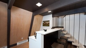 Une cuisine moderne avec un plan de travail blanc, des tabourets en bois et une image d’ours accrochée au mur.