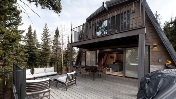 Une maison moderne à deux étages, dotée d’une terrasse, de mobilier d’extérieur et d’une grande porte-fenêtre coulissante.