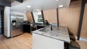 Une cuisine moderne dotée d’un îlot central, d’appareils électroménagers en acier inoxydable et d’un mur d’accent en bois.