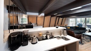 Une cuisine moderne dotée d’un grand îlot central, d’appareils électroménagers intégrés et offrant une vue sur l’extérieur.