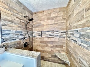A shower with a handheld showerhead and a wall-mounted showerhead, surrounded by a stone mosaic backsplash. - Wearadise Mountain Views Home features Hot Tub and Fire Pit by RedAwning (Sevierville)