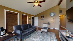 A living room with a grey sofa, a patterned rug, a ceiling fan, a clock, and a small table with decorative items. - Wearadise Mountain Views Home features Hot Tub and Fire Pit by RedAwning (Sevierville)