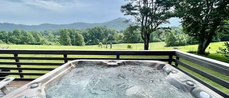 A hot tub on a deck with a view of a green landscape and mountains.
