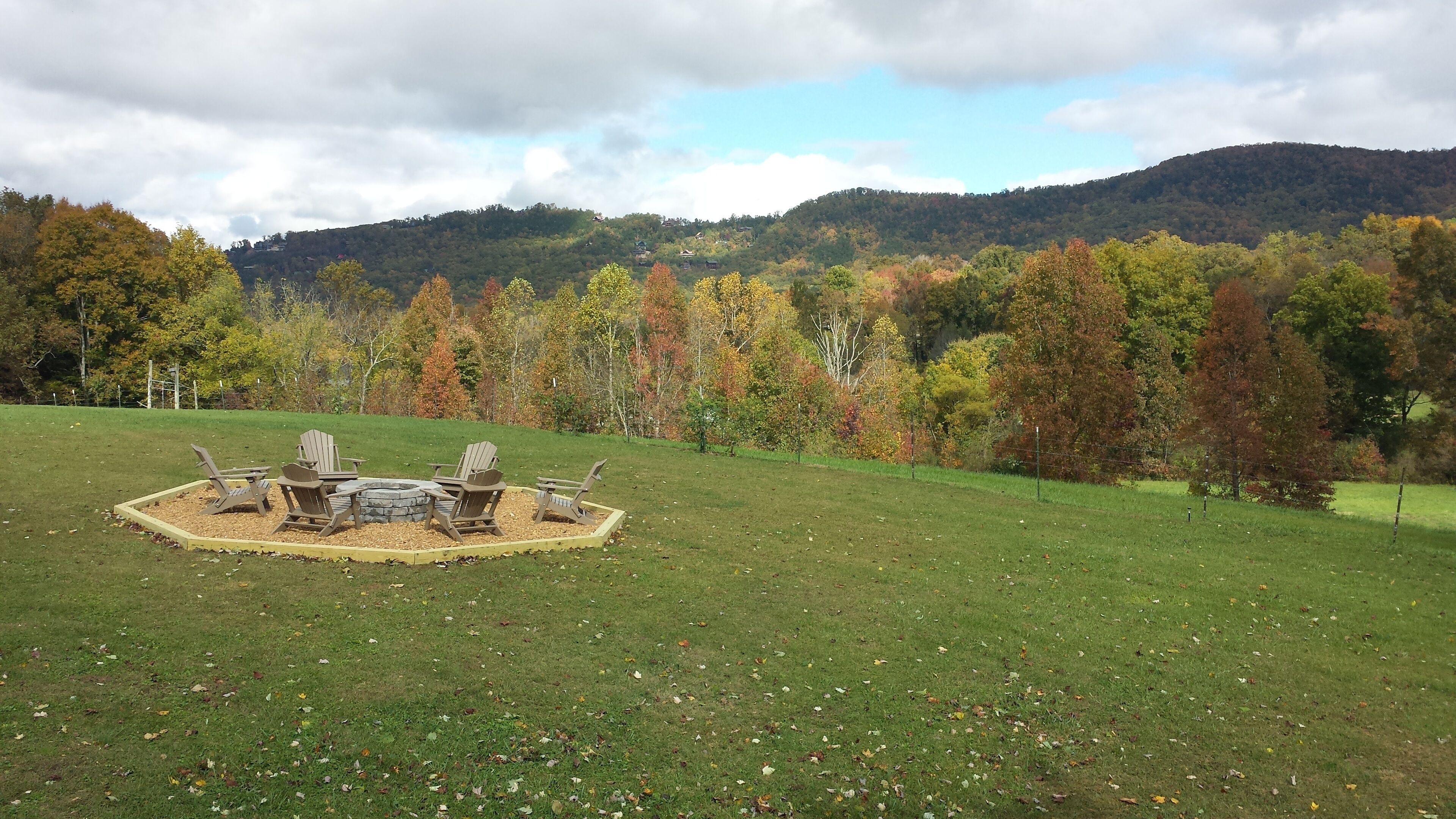 A grassy field with a circular seating area and a stone fire pit.