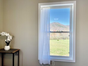 A room with a window overlooking a grassy field and a mountain.