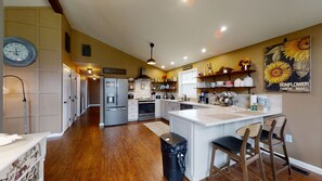 A kitchen with a central island, stainless steel appliances, wooden flooring, and a wall clock.
