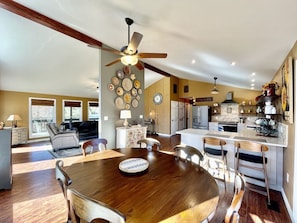 A spacious living area with a large wooden dining table, a ceiling fan, and a kitchen with modern appliances.