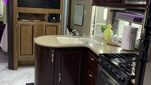 A compact kitchen with a built-in stove, a sink, and a microwave. There is a small island with a countertop and a chair. The kitchen has wooden cabinets and a marble floor. - Beautiful vacation mobile home at the Florida keys. (Key Largo)