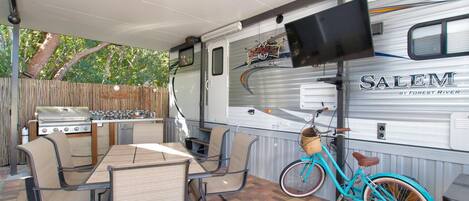 A covered outdoor area with a table and chairs, a grill, and a bicycle.