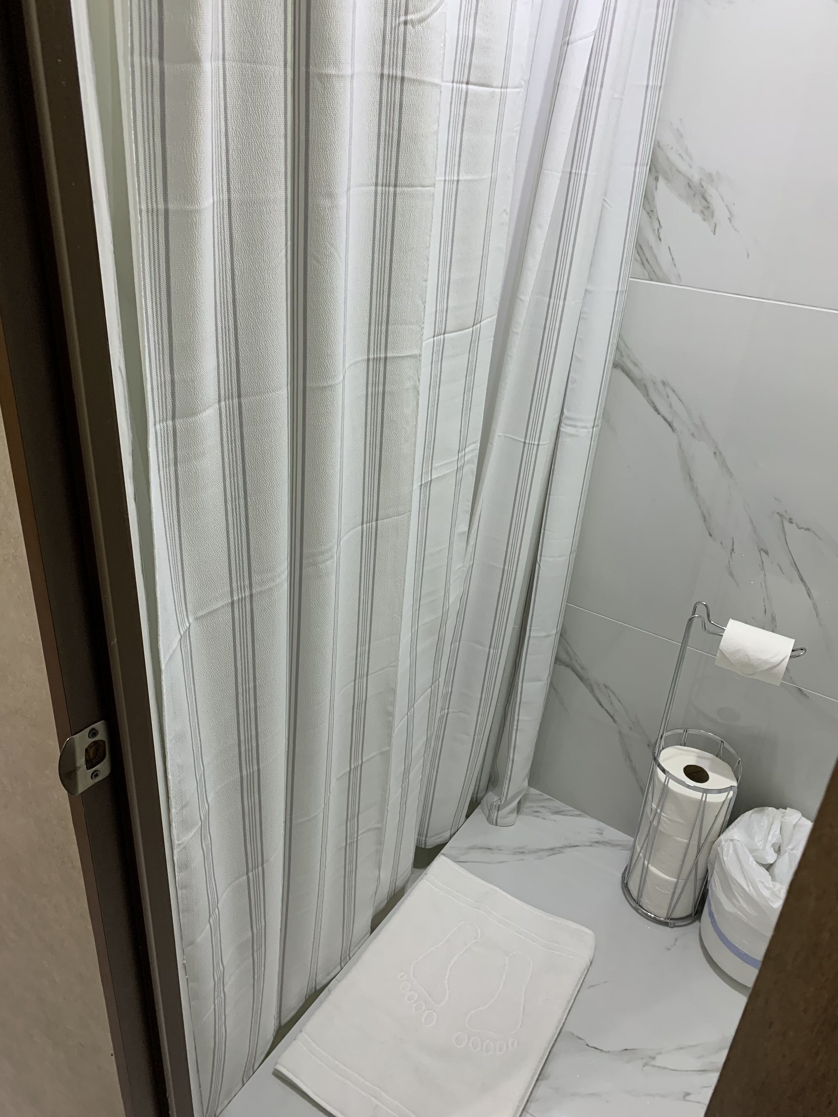 Et badeværelse med badeforhæng, toiletpapirholder og væg med marmorfliser.