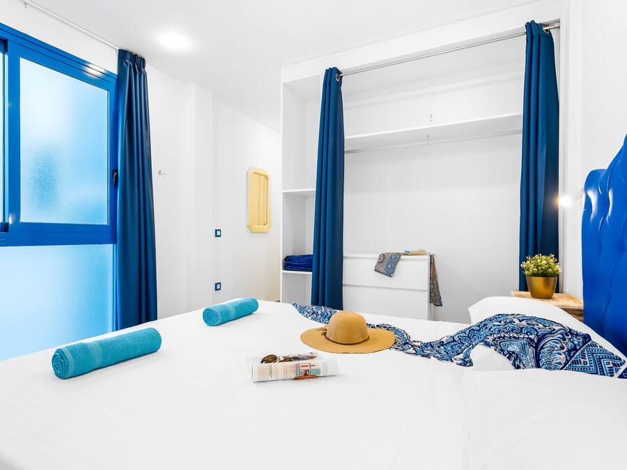 Habitación de hotel con cama, ventana, armario y una mesita con una planta.