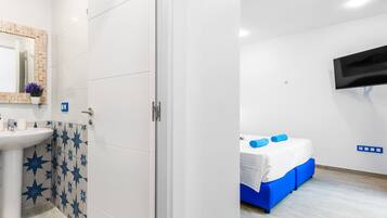 A modern hotel room with a white sink, blue star-patterned tiles, a bed with blue bedding, and a mounted TV.