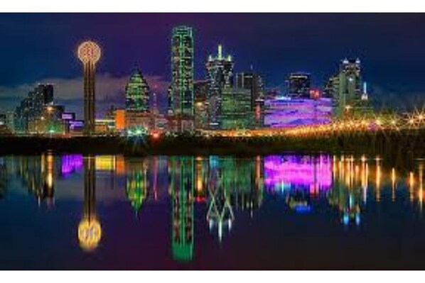A nighttime cityscape with illuminated buildings reflected in a body of water.