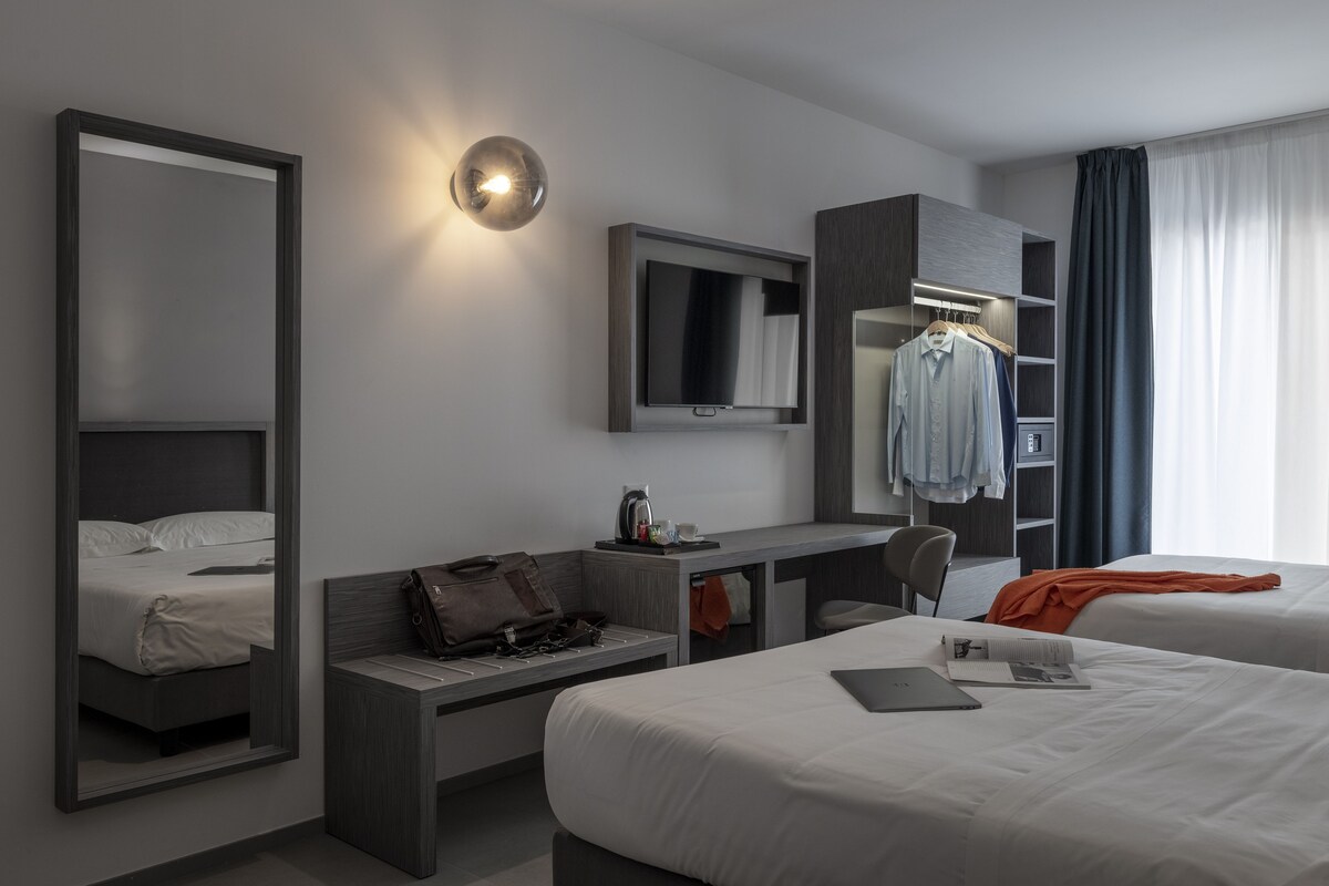 A modern hotel room with a large bed, a desk, a TV, and a wardrobe.
