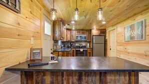 Une cuisine rustique aux murs en bois, avec un îlot central doté de tabourets, un four à micro-ondes et un réfrigérateur.