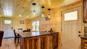Un intérieur en bois avec un îlot central, des chaises de salle à manger, une porte et une fenêtre.