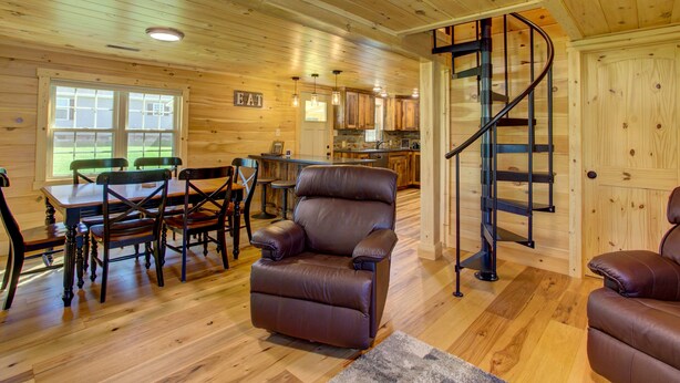 L’intérieur d’une cabane en bois comprend un coin repas, un fauteuil inclinable, une cuisine et un escalier en colimaçon.