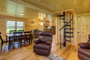 L’intérieur d’une cabane en bois comprend un coin repas, un fauteuil inclinable, une cuisine et un escalier en colimaçon.