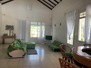 A spacious living room with a large window, a television, and a dining area with a table and chairs.