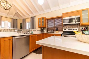 A modern kitchen with wooden cabinets, a stainless steel dishwasher, a built-in oven, and a microwave. - Paradise Villa|Gated|Pool|Richmond (Ocho Rios)