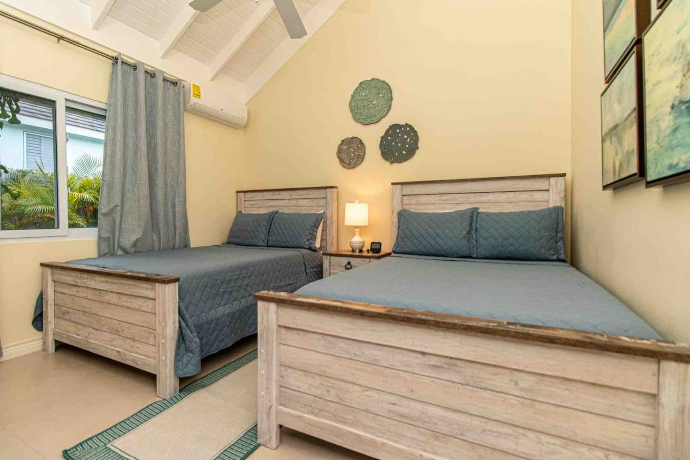 Un dormitorio con dos camas de madera, una mesita de noche con lámpara y un ventanal con cortinas.
