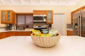 A modern kitchen with wooden cabinets, a stainless steel refrigerator, a built-in oven, and a large island with a bowl of chips. - Paradise Villa|Gated|Pool|Richmond (Ocho Rios)