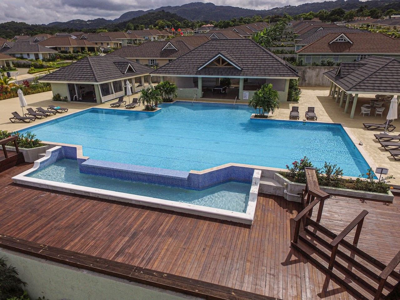 Un resort con una amplia piscina, sillas de descanso y una terraza de madera.