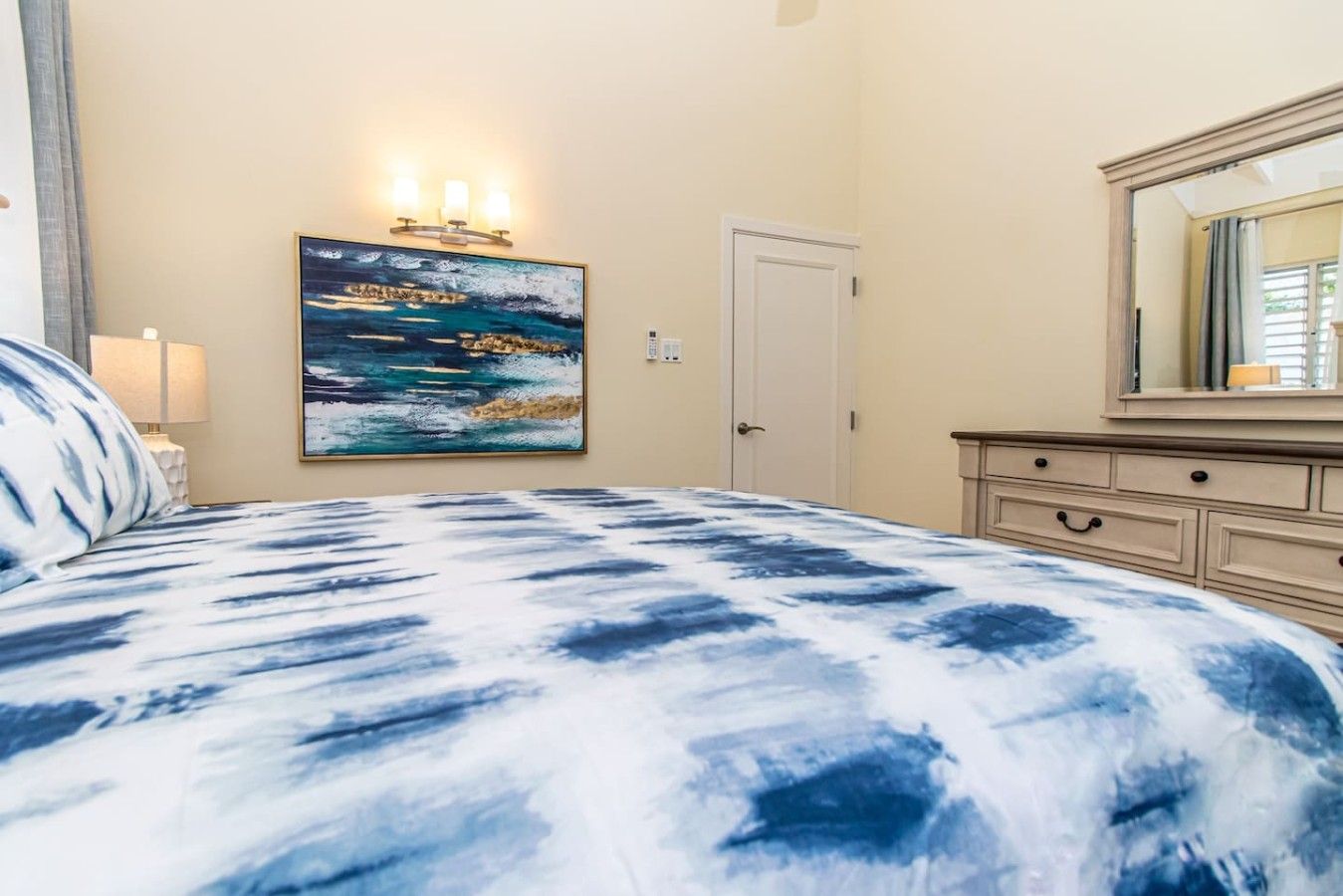A bedroom with a bed, a painting, a dresser, and a door.