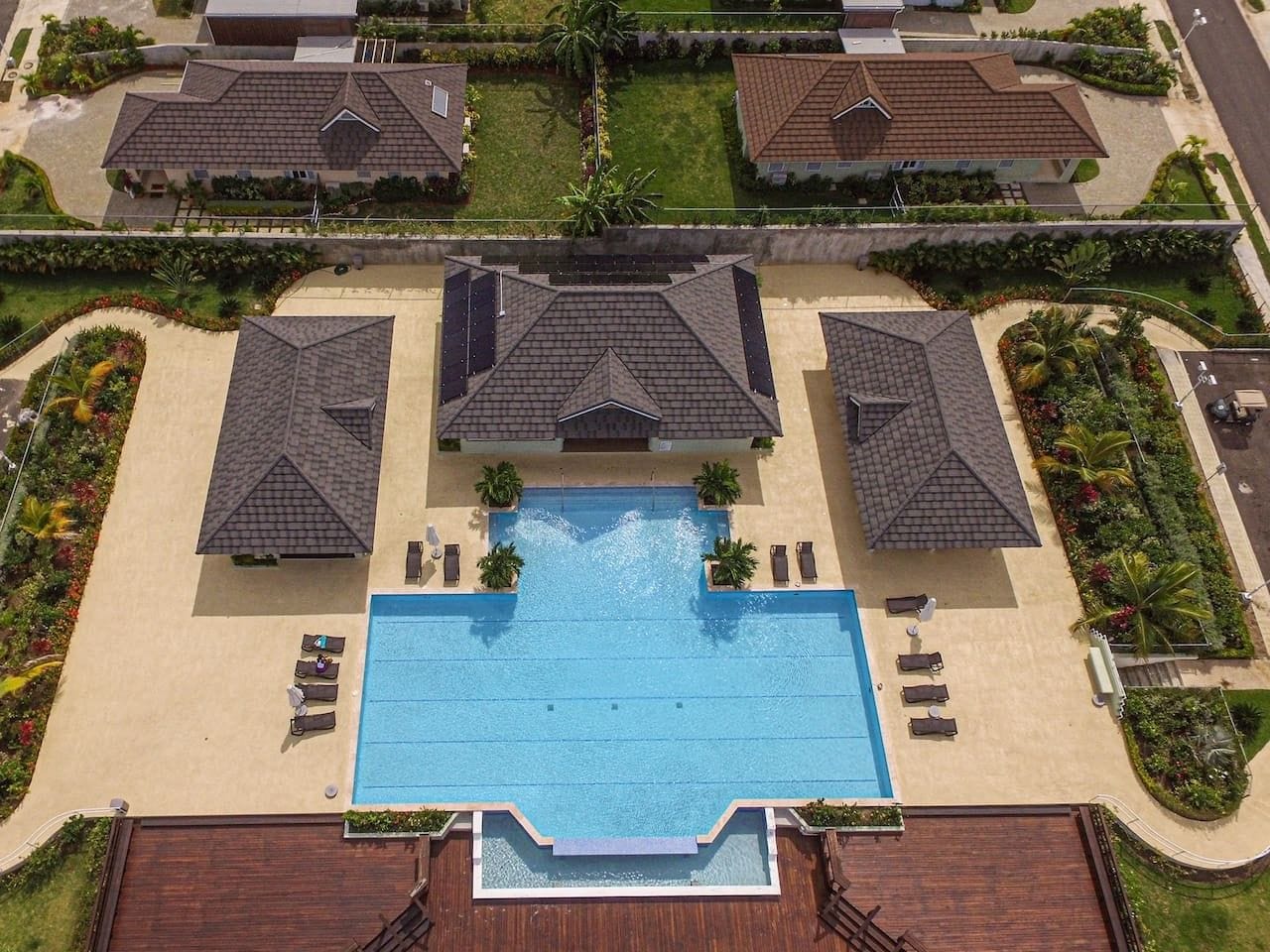 A residential area with a central swimming pool, surrounded by houses with sloped roofs, and a landscaped garden.