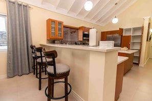 A kitchen with a central island, bar stools, wooden cabinets, and a refrigerator. - Paradise Villa|Gated|Pool|Richmond (Ocho Rios)