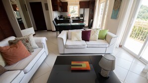 Ein modernes Wohnzimmer mit einem weißen Sofa, einem schwarzen Couchtisch und einer Küche im Hintergrund.