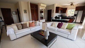 Ein modernes Wohnzimmer mit zwei weißen Sofas, einem schwarzen Couchtisch und einer Küche im Hintergrund.