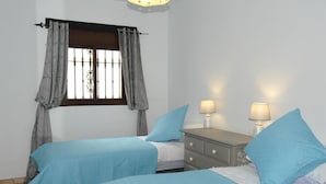 A bedroom with two beds, a nightstand with two lamps, a window with curtains, and a wall-mounted light fixture. - Finca La Cantarera Tarifa -Poniente apartment - Reconnect with yourself + nature (Tarifa)
