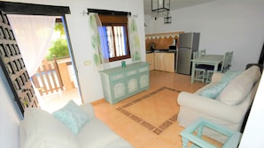 A compact living space with a sofa, a small table, a kitchen area with a refrigerator and stove, and a sliding door leading to an outdoor area. - Finca La Cantarera Tarifa -Poniente apartment - Reconnect with yourself + nature (Tarifa)