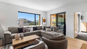 A modern living room with a sectional sofa, a coffee table, and a view of a mountain landscape through large windows. - Mountain Views Penthouse - Apartment 22 (Queenstown)