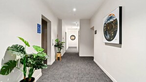 A hallway with a wheelchair-accessible sign, potted plants, and artwork on the walls. - Mountain Views Penthouse - Apartment 22 (Queenstown)