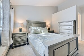 Ein Schlafzimmer mit einem Bett, zwei Nachttischen, einer Kommode und einem Fenster mit Vorhängen.