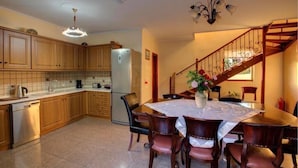 A kitchen with wooden cabinets, a stainless steel refrigerator, a dining table with chairs, and a staircase with a railing. - Villa Thalassa Thea (Corfu)
