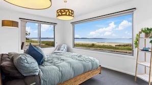 A bedroom with a large window, a bed, a chair, and a plant shelf. - Seven Mile Beach House Surf Hike Golf (Seven Mile Beach)