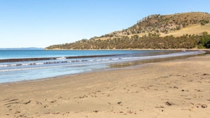 A beach with clear blue water, sandy shore, and a hill with trees in the background. - Seven Mile Beach House Surf Hike Golf (Seven Mile Beach)