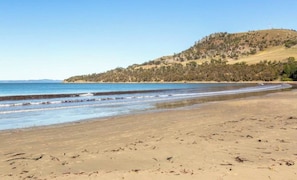 Ein Strand mit sandigem Ufer, sanften Wellen und einer bewaldeten Hügelkette im Hintergrund.