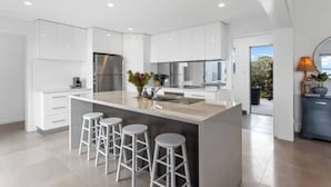 A modern kitchen with white cabinetry, a large island with stools, and a view to the outdoors. - Seven Mile Beach House Surf Hike Golf (Seven Mile Beach)