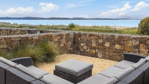 A stone-walled outdoor seating area with wicker furniture and a view of the sea. - Seven Mile Beach House Surf Hike Golf (Seven Mile Beach)