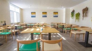Een ruime eetruimte met meerdere tafels en stoelen, grote ramen en decoratieve wandkunst.