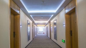 Een lange, smalle hotelgangen met houten deuren aan beide zijden, een bekleed vloeroppervlak en een plafond met inbouwspots.