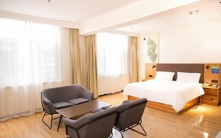 A hotel room with a bed, a desk, two chairs, and a nightstand with a lamp.