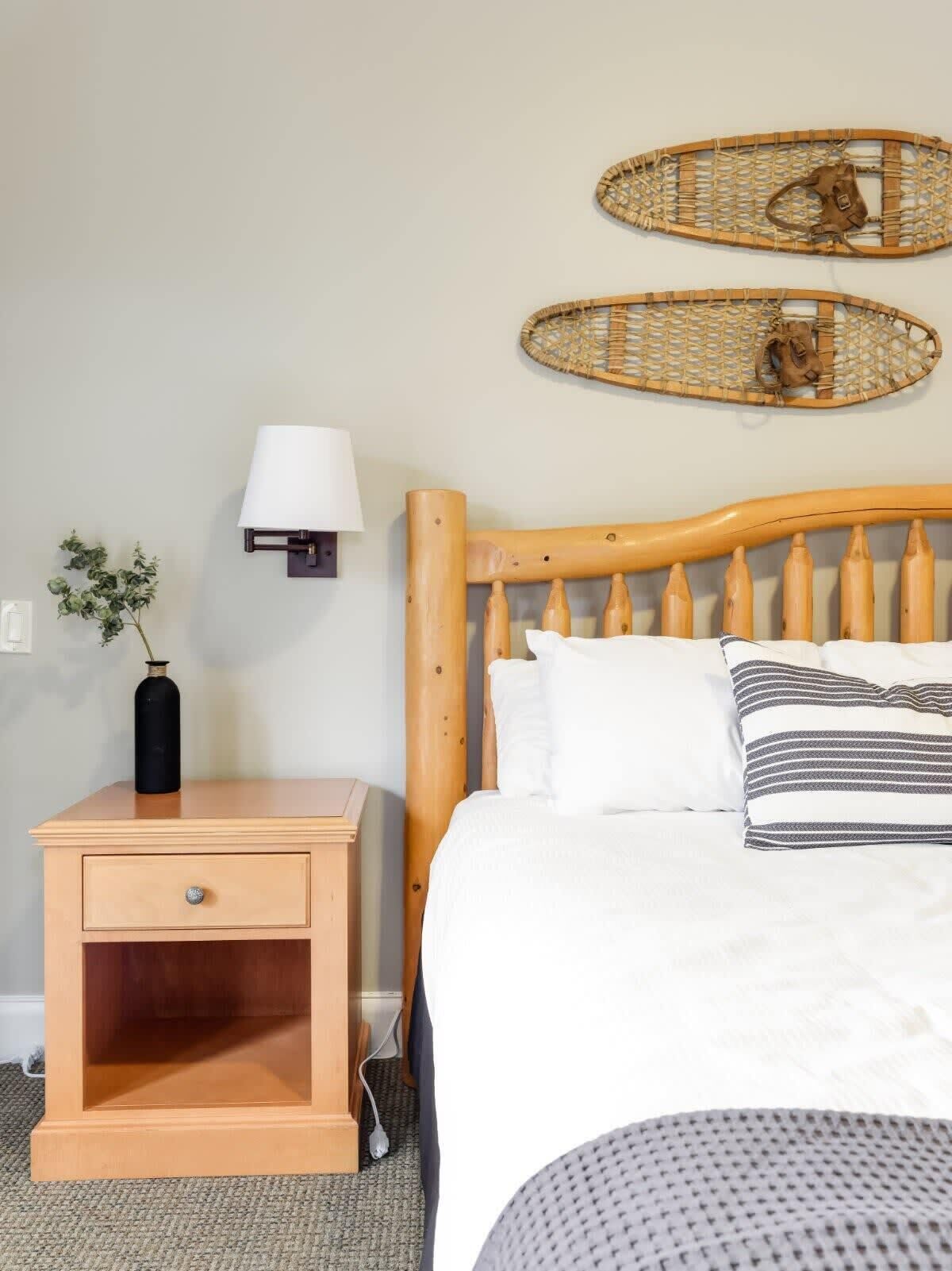 Ein ordentlich eingerichtetes Schlafzimmer mit einem hölzernen Bett, einem Nachttisch mit Lampe und zwei gewobenen Wanddekorationen.