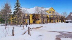 A yellow multi-story building with balconies, surrounded by snow-covered ground and trees. - All Season Ski in/Out Chalets at Calabogie Peaks (Calabogie)