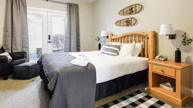A neatly arranged bedroom with a bed, bedside tables, a chair, and a view through a window. - All Season Ski in/Out Chalets at Calabogie Peaks (Calabogie)